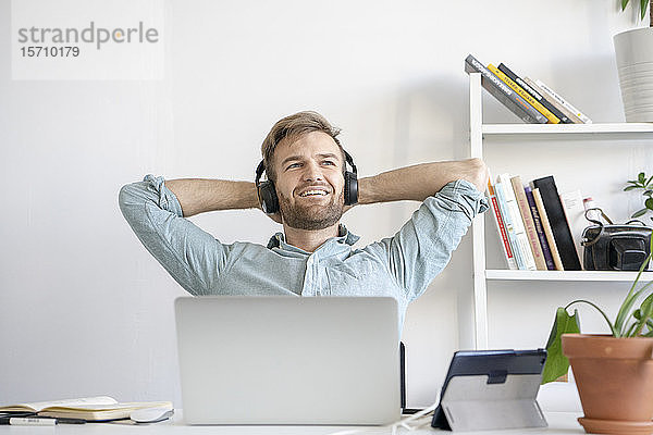 Lächelnder Mann hört Musik am Schreibtisch im Büro