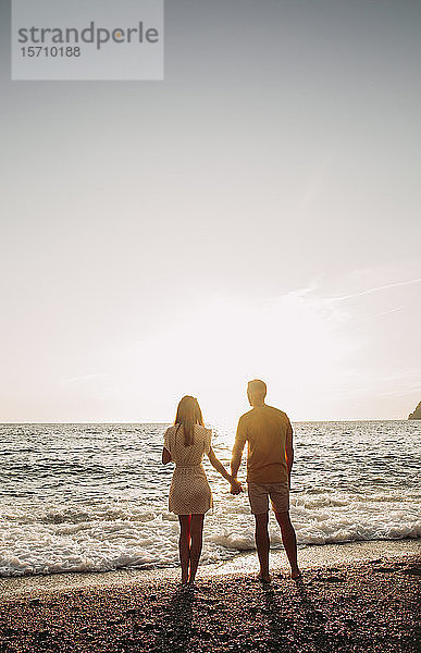 Rückansicht eines jungen Paares am Strand bei Sonnenuntergang