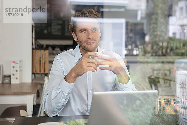 Junger Geschäftsmann mit Kaffeetasse und Laptop in einem Cafe