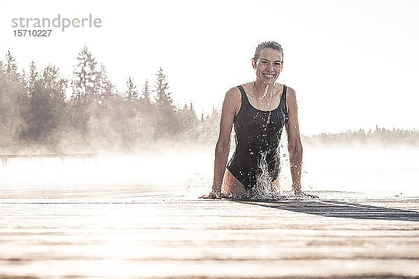 Glückliche Frau im schwarzen Badeanzug badet im Morgennebel in einem See