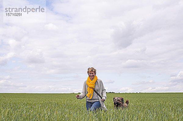 Glückliche Frau geht mit Hund auf einem Feld spazieren