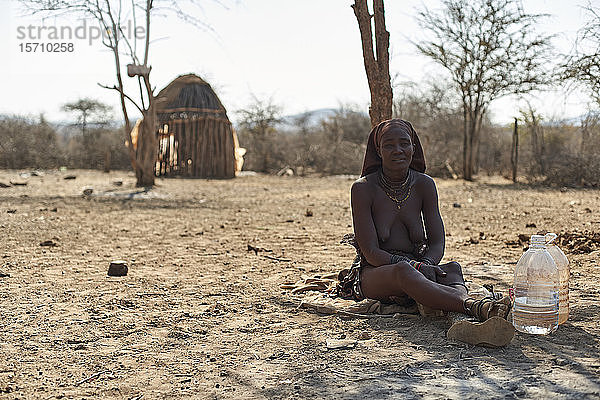 Himba-Frau sitzt auf sandigem Boden in ihrem Dorf  Opuwo  Namibia