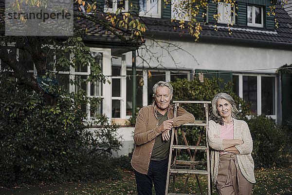 Porträt eines älteren Ehepaares mit einer Leiter im Garten ihres Hauses