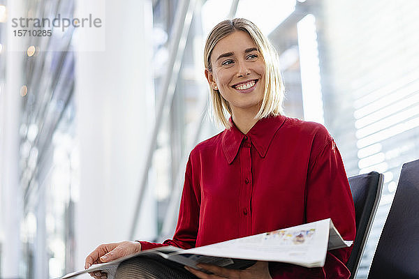 Lächelnde junge Geschäftsfrau mit Zeitung sitzt im Wartebereich