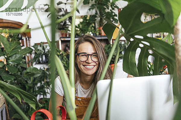 Porträt einer glücklichen jungen Frau mit Laptop  umgeben von Pflanzen