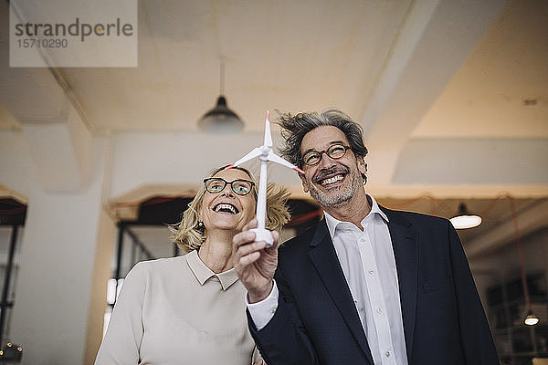 Glücklicher Geschäftsmann und Geschäftsfrau  die ein Windturbinenmodell im Amt halten