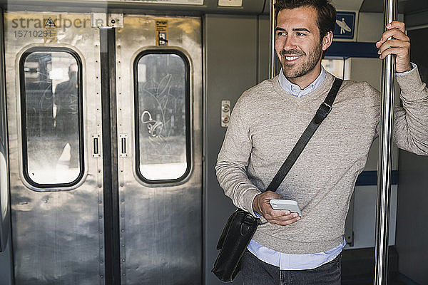 Lächelnder junger Mann mit Smartphone im Zug