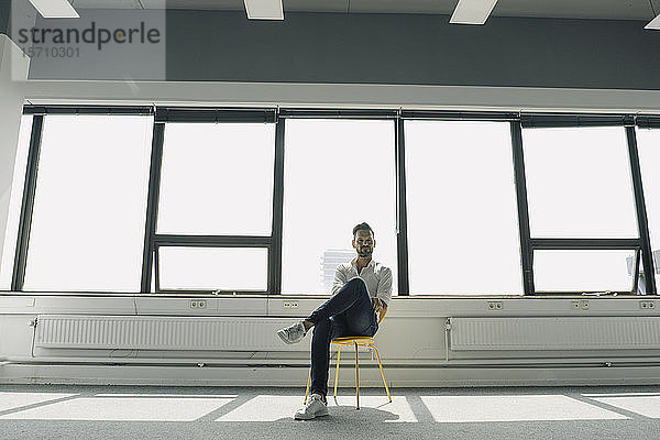 Reifer Geschäftsmann sitzt auf gelbem Stuhl in leerem Büro