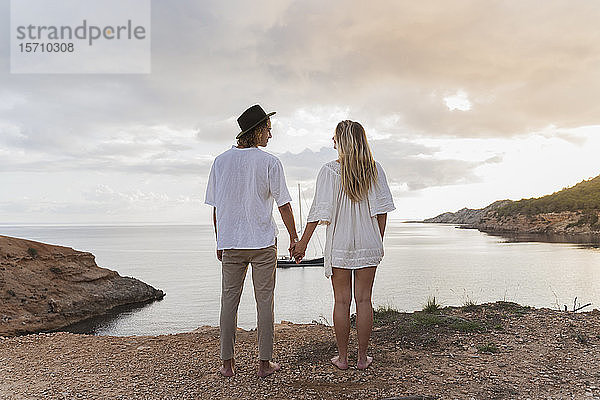 Rückansicht eines jungen verliebten Paares vor dem Meer stehend  Ibiza  Balearen  Spanien