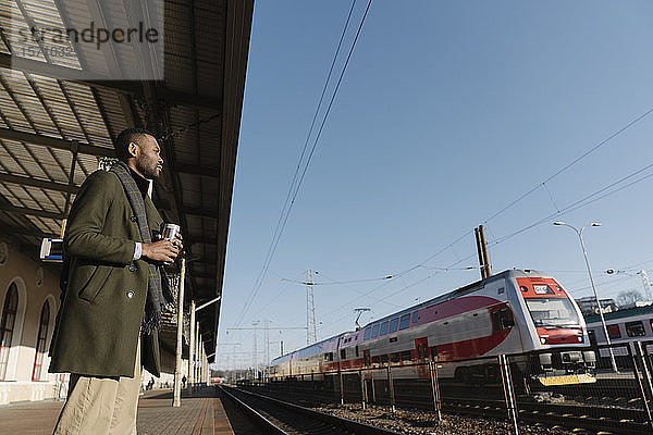 Stilvoller Mann mit wiederverwendbarem Becher wartet auf den Zug