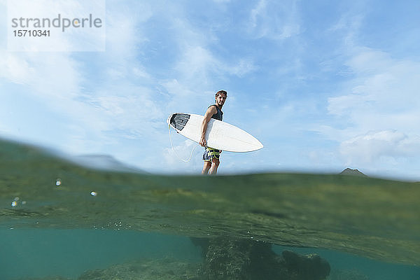 Surfer mit seinem Surfbrett in der Hand  auf Stein stehend  Insel Sumbawa  Indonesien  über-unteres Bild
