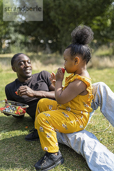 Vater und Tochter essen Obst auf einer Wiese in einem Park