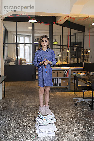 Mädchen steht auf einem Bücherstapel im Büro