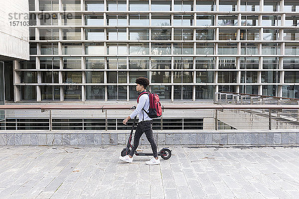 Junger Mann geht mit einem E-Scooter in der Stadt