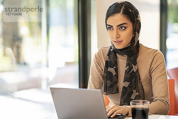 Junge Frau trägt Kopftuch mit Laptop in einem Café