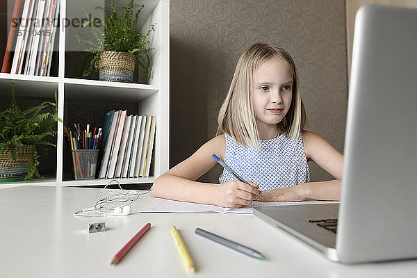 Mädchen  das zu Hause am Tisch sitzt  Hausaufgaben macht und einen Laptop benutzt