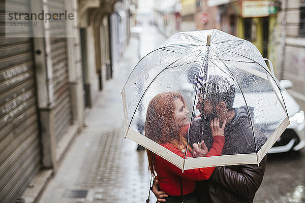 Verliebtes Ehepaar unter transparentem Schirm in der Stadt