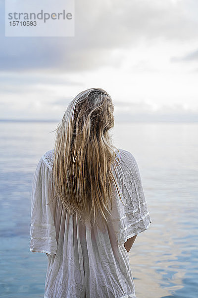 Rückenansicht einer jungen blonden Frau  die vor dem Meer steht  Ibiza  Balearen  Spanien