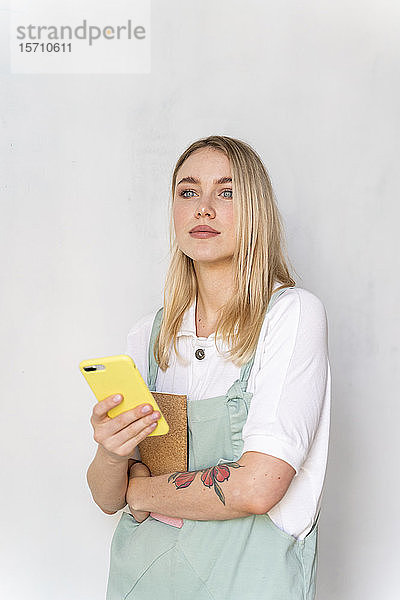 Porträt einer jungen Frau mit Notebook und Handy in der Hand