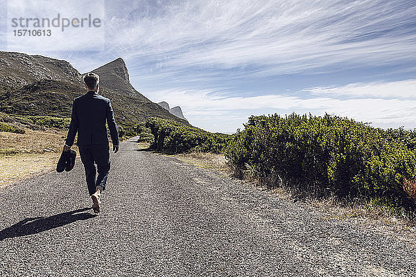 Rückansicht eines Geschäftsmannes  der barfuss auf einer Landstrasse geht  Cape Point  Western Cape  Südafrika