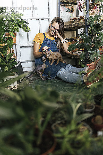 Junge Frau mit Dinosaurier-Figur  die in einem kleinen Laden mit Pflanzen auf dem Boden sitzt