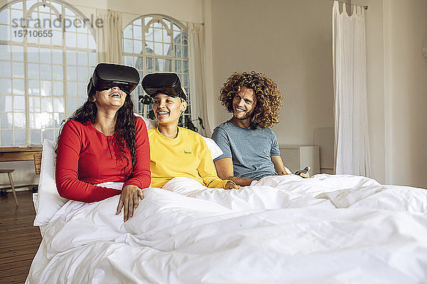 Glückliche Freunde haben Spaß mit VR-Brillen im Bett zu Hause