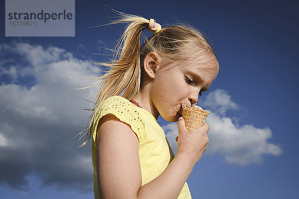 Porträt eines blonden Mädchens  das Eis gegen den Himmel isst