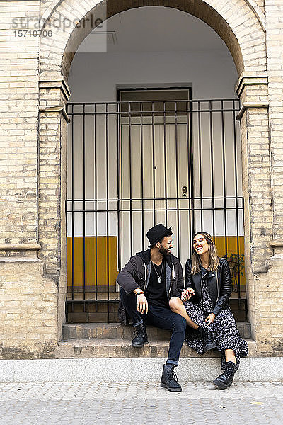 Lachendes junges Paar sitzt auf einer Treppe im Freien