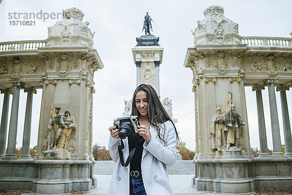 Lächelnde Frau mit einer Kamera vor dem Alfonso-XII-Denkmal im Park El Retiro  Madrid  Spanien