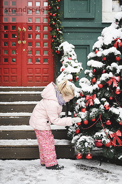 Kleines Mädchen beobachtet Weihnachtskugeln am Weihnachtsbaum im Freien