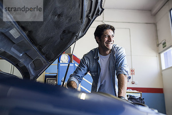 Lächelnder Mann arbeitet mit dem Motor eines Autos im Reparaturdienst und schaut weg