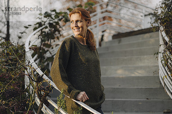Glückliche Frau steht auf der Treppe in ihrem Garten und lächelt