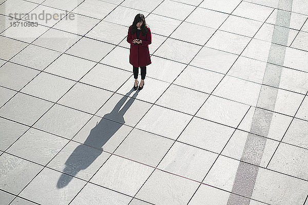 Geschäftsfrau benutzt Smartphone und steht auf Betonboden
