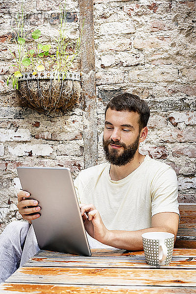 Junger Mann sitzt im Hinterhof und benutzt ein digitales Tablett