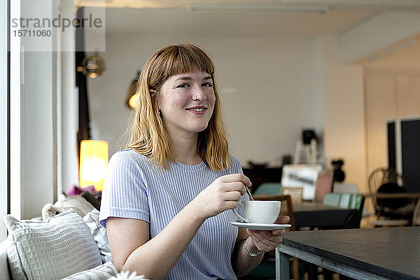 Porträt einer erdbeerblonden jungen Frau mit Nasenpiercing bei einer Tasse Kaffee in einem Cafe