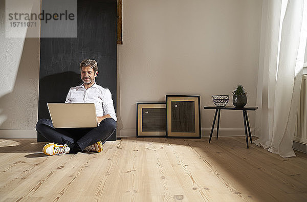 Entspannter reifer Mann sitzt zu Hause mit Laptop auf dem Boden