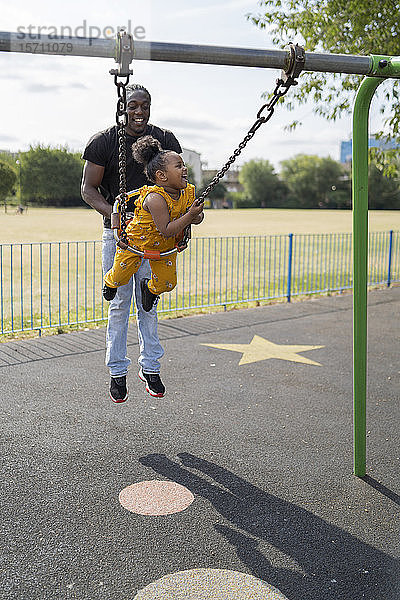 Vater mit glücklicher Tochter schaukelt auf einem Spielplatz