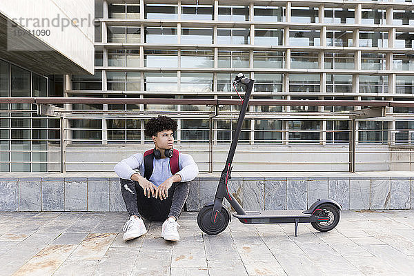 Junger Mann mit E-Scooter in der Stadt sitzend