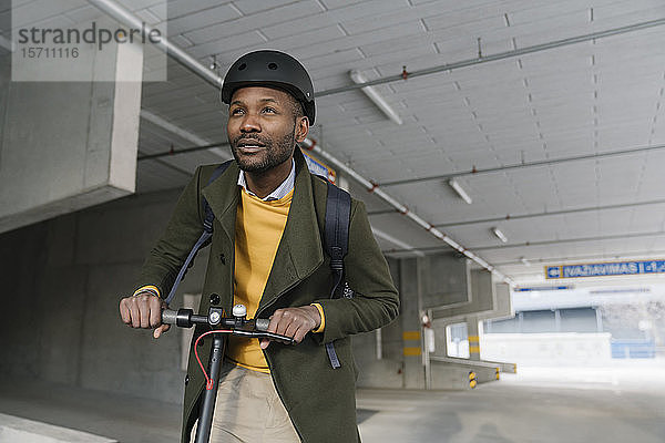 Porträt eines stilvollen Mannes mit Helm und Roller in der Stadt