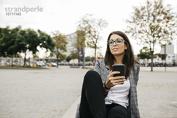 Junge Geschäftsfrau mit Smartphone  die in der Stadt auf einer Bank sitzt