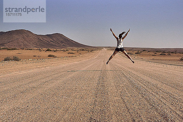 Frau springt mitten auf einen Feldweg  Damaraland  Namibia