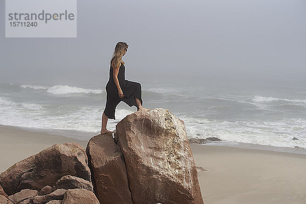 Auf einem Felsen stehende Frau mit Blick auf den Ozean  Cape Cross  Namibia