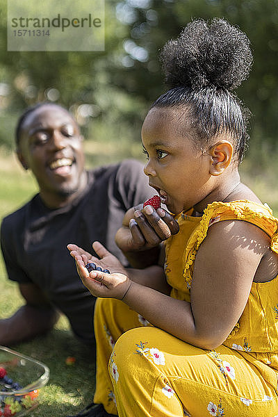 Glückliche Vater und Tochter essen Obst auf einer Wiese in einem Park