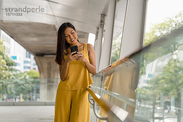 Porträt einer modischen Frau auf einer Terrasse mit Blick auf ihr Handy