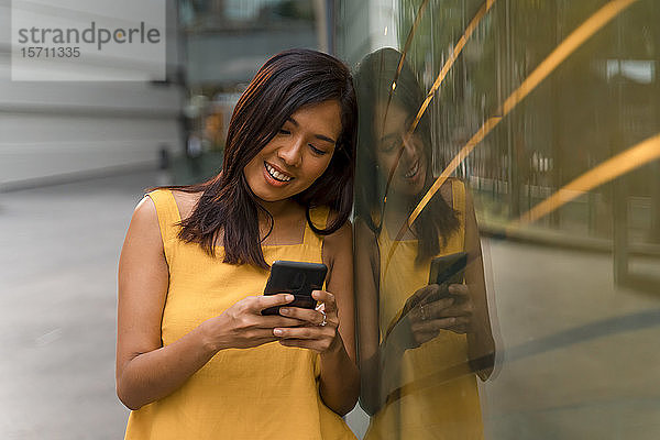 Porträt einer lächelnden jungen Frau  die auf ein Smartphone schaut
