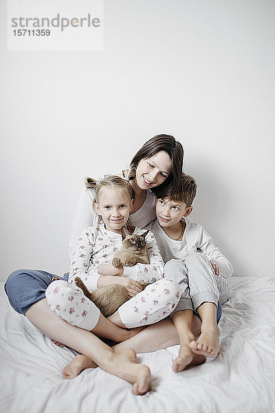 Mutter mit zwei Kindern und einer auf dem Bett sitzenden Katze
