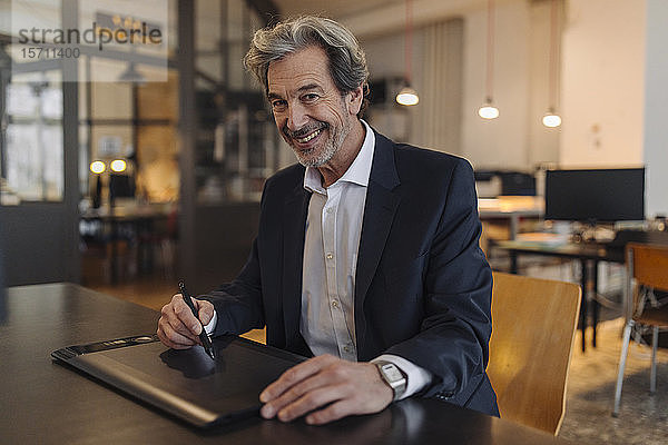 Portrait eines lächelnden älteren Geschäftsmannes mit Grafiktablett am Schreibtisch im Büro