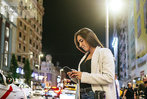 Frau benutzt ihr Smartphone nachts auf der Straße