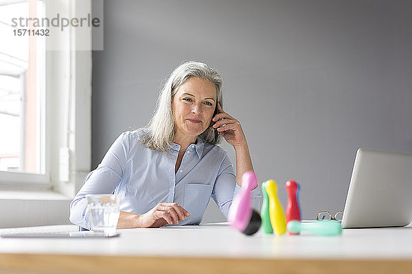 Reife Geschäftsfrau am Telefon spielt mit Stecknadeln auf dem Schreibtisch im Büro