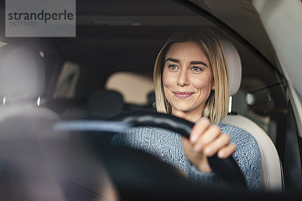 Porträt einer lächelnden jungen Frau am Steuer eines Autos